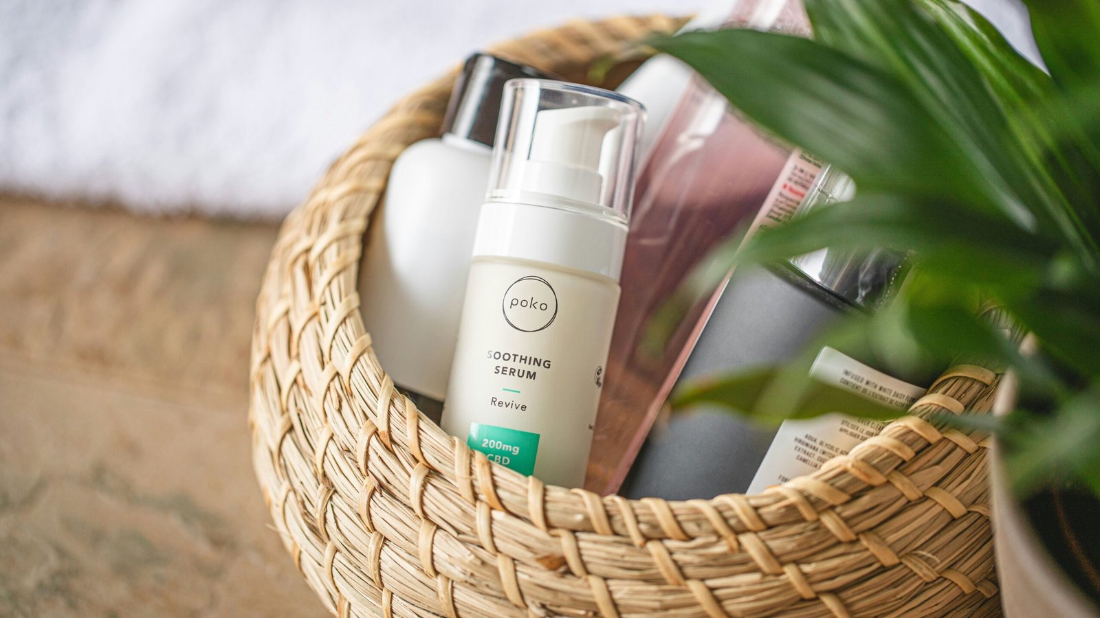 Skincare products including a soothing serum bottle arranged in a woven basket outdoors